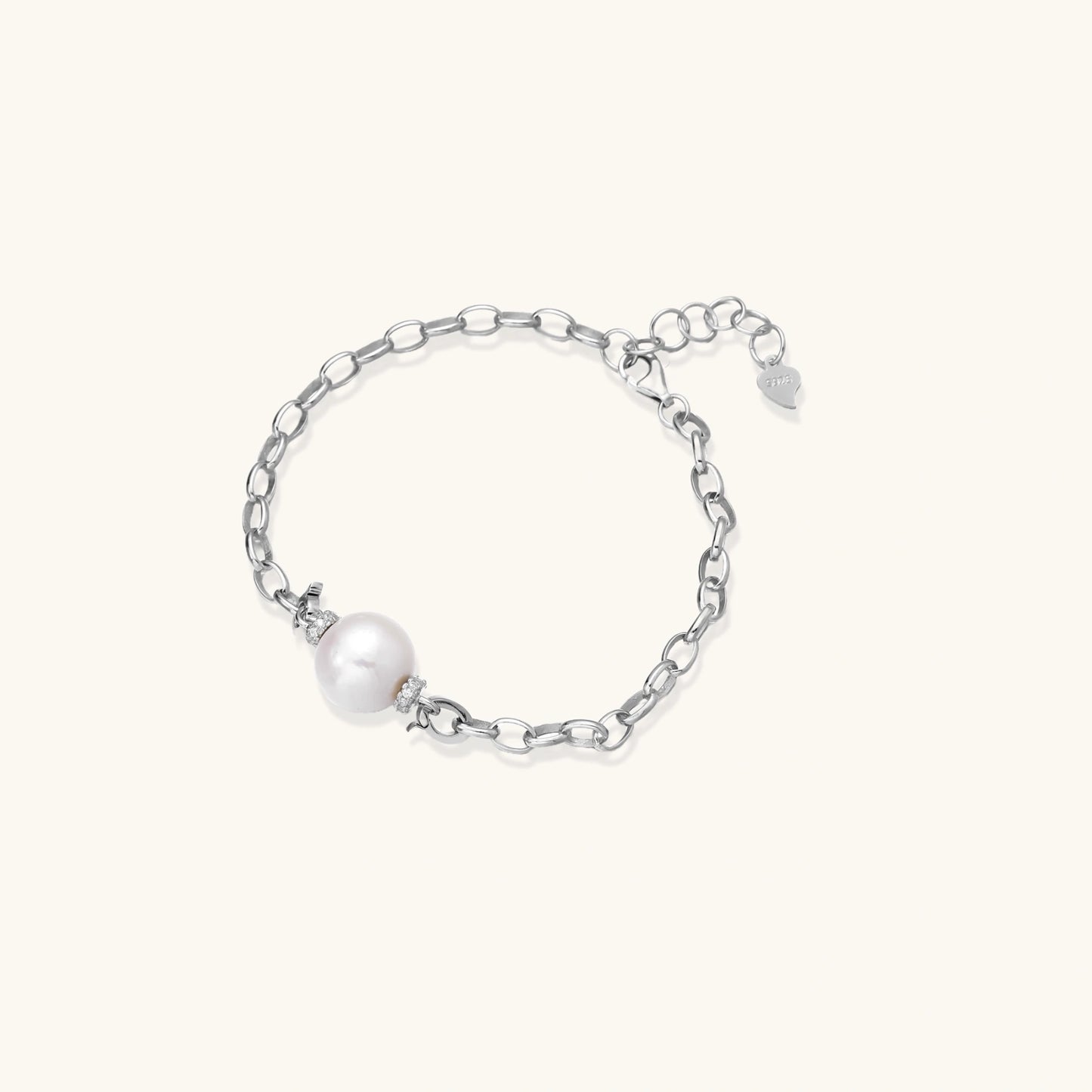 Rhodium-plated silver chain bracelet with single white freshwater pearl and heart charm clasp on cream background