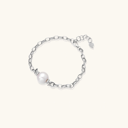 Rhodium-plated silver chain bracelet with single white freshwater pearl and heart charm clasp on cream background