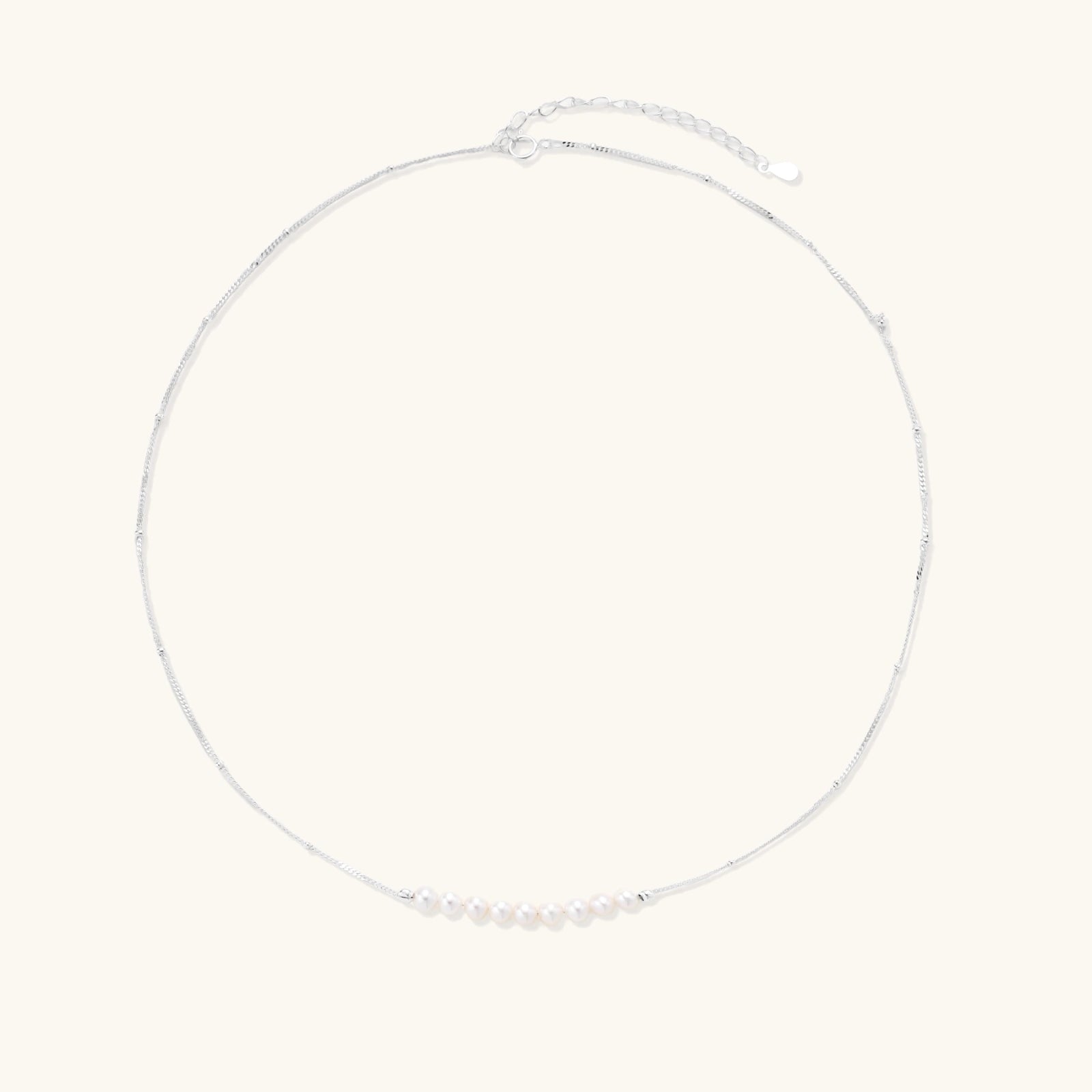 Delicate sterling silver chain necklace with small freshwater pearls arranged in a curved smile arc on cream background.
