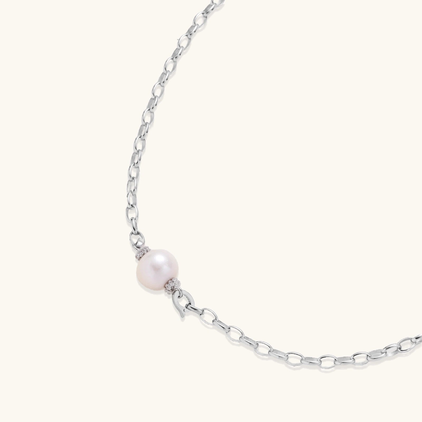 Dainty rhodium-plated silver chain necklace with centered 10mm freshwater pearl and crystal accents on cream background