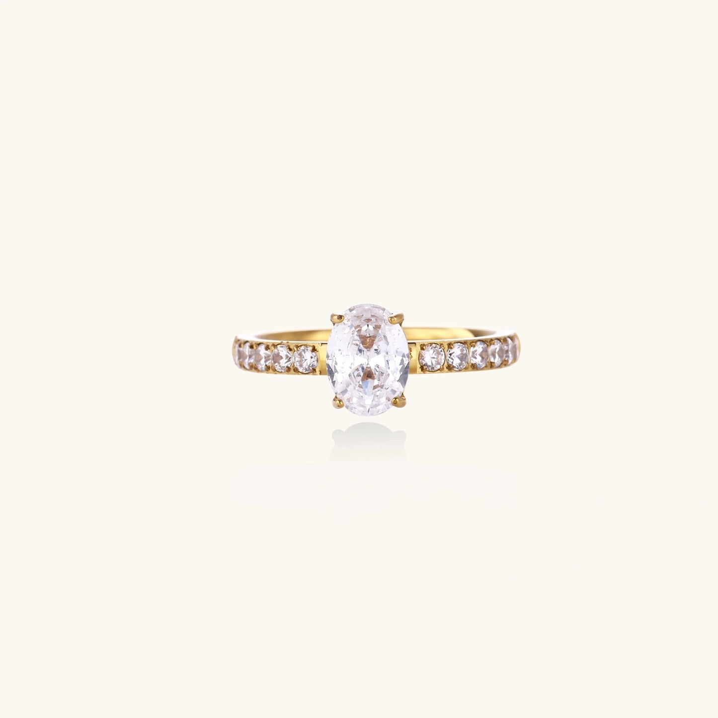Gold-plated solitaire ring with oval zirconia center stone and pavé band on cream background