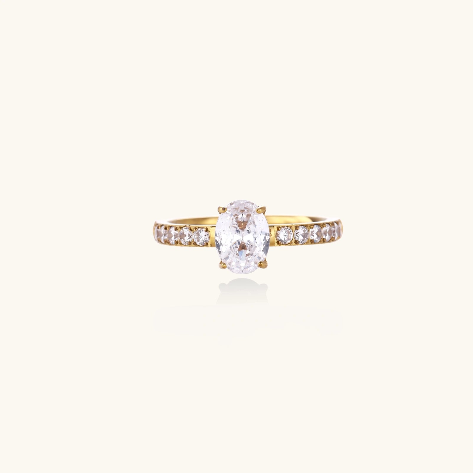 Gold-plated solitaire ring with oval zirconia center stone and pavé band on cream background
