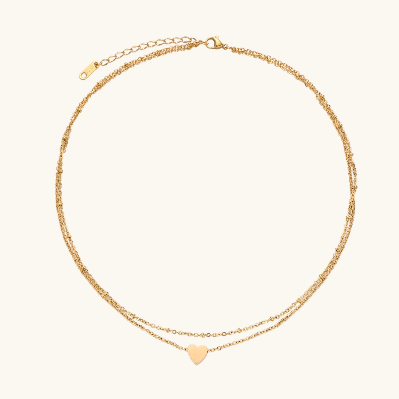 Delicate double-chain gold necklace with tiny heart pendant on cream background