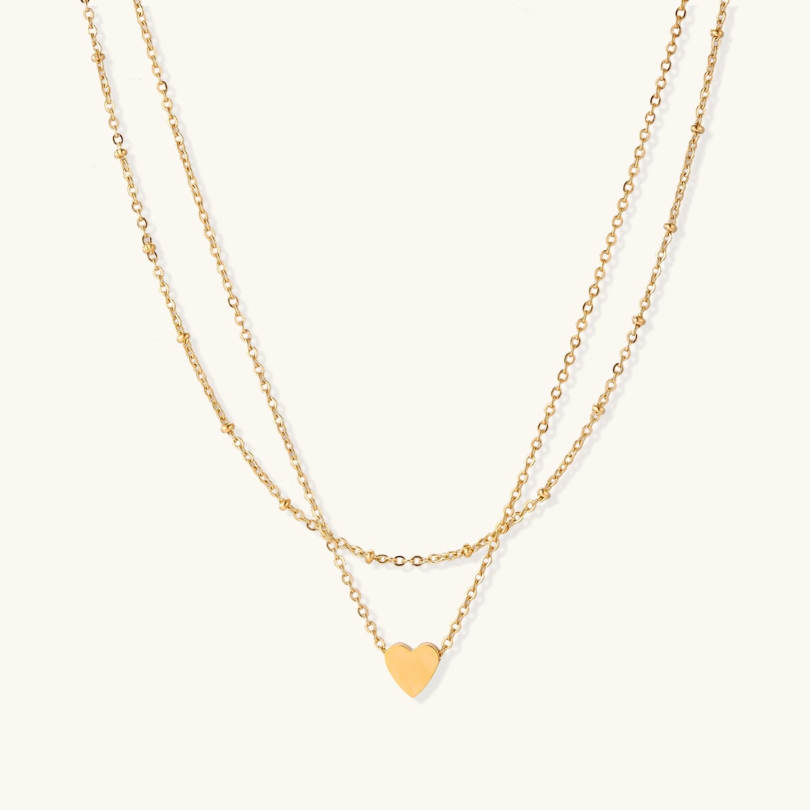Delicate double-chain gold necklace with tiny heart pendant on cream background