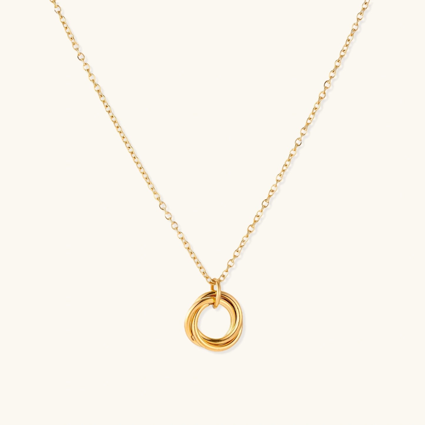 Delicate gold-plated necklace with three interlocking circle rings forming a minimalist knot pendant on cream background