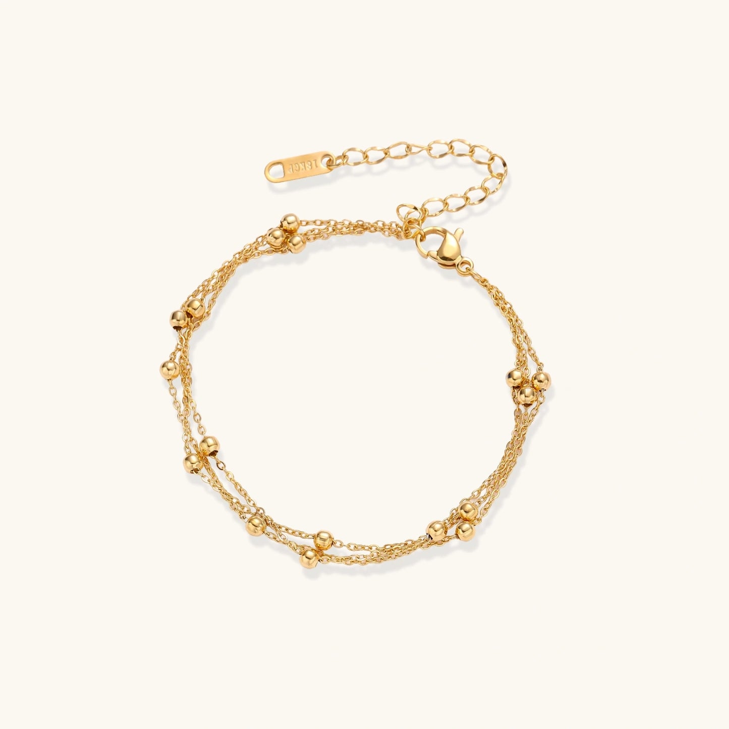 Three-strand gold-plated bracelet with clustered ball beads and adjustable clasp on cream background