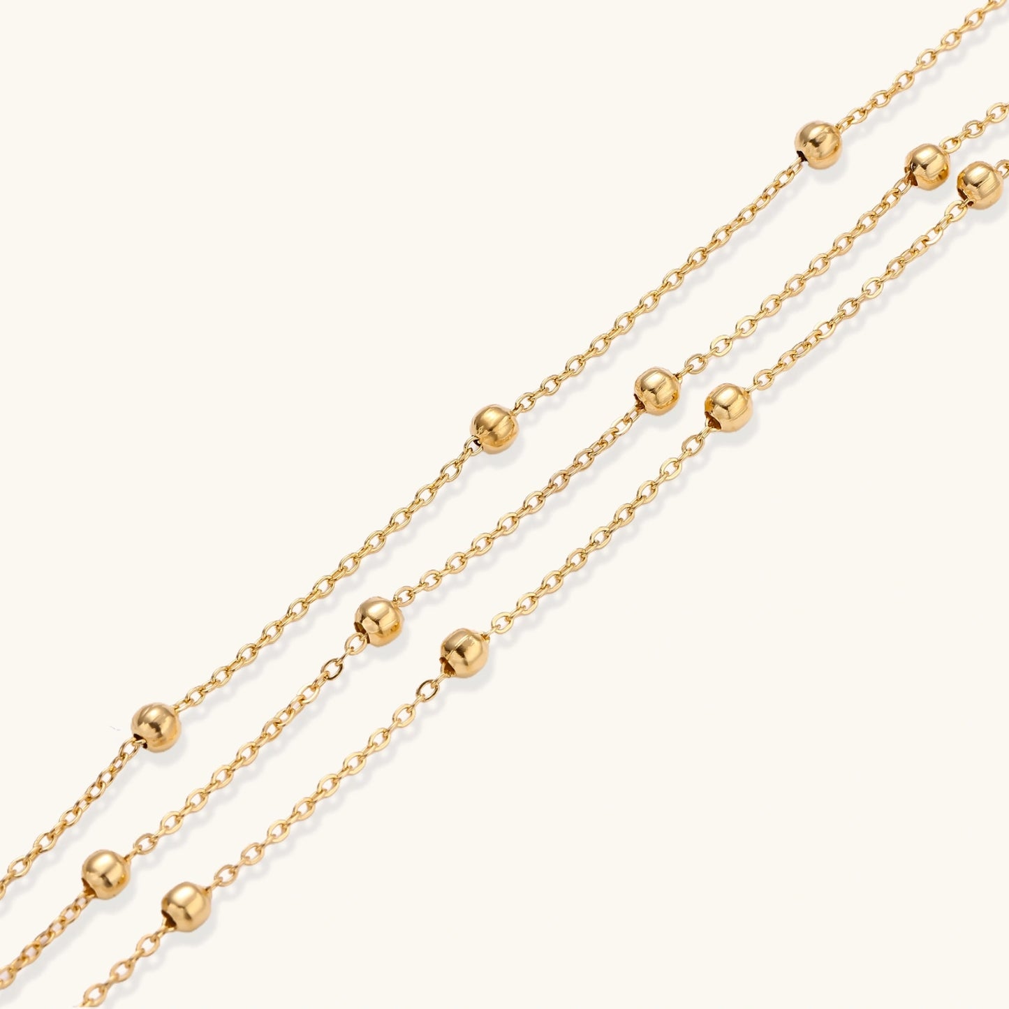 Three-strand gold-plated bracelet with clustered ball beads and adjustable clasp on cream background