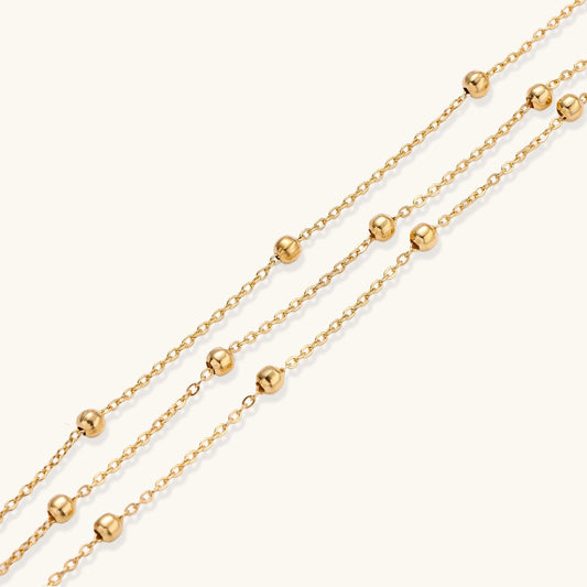 Three-strand gold-plated bracelet with clustered ball beads and adjustable clasp on cream background