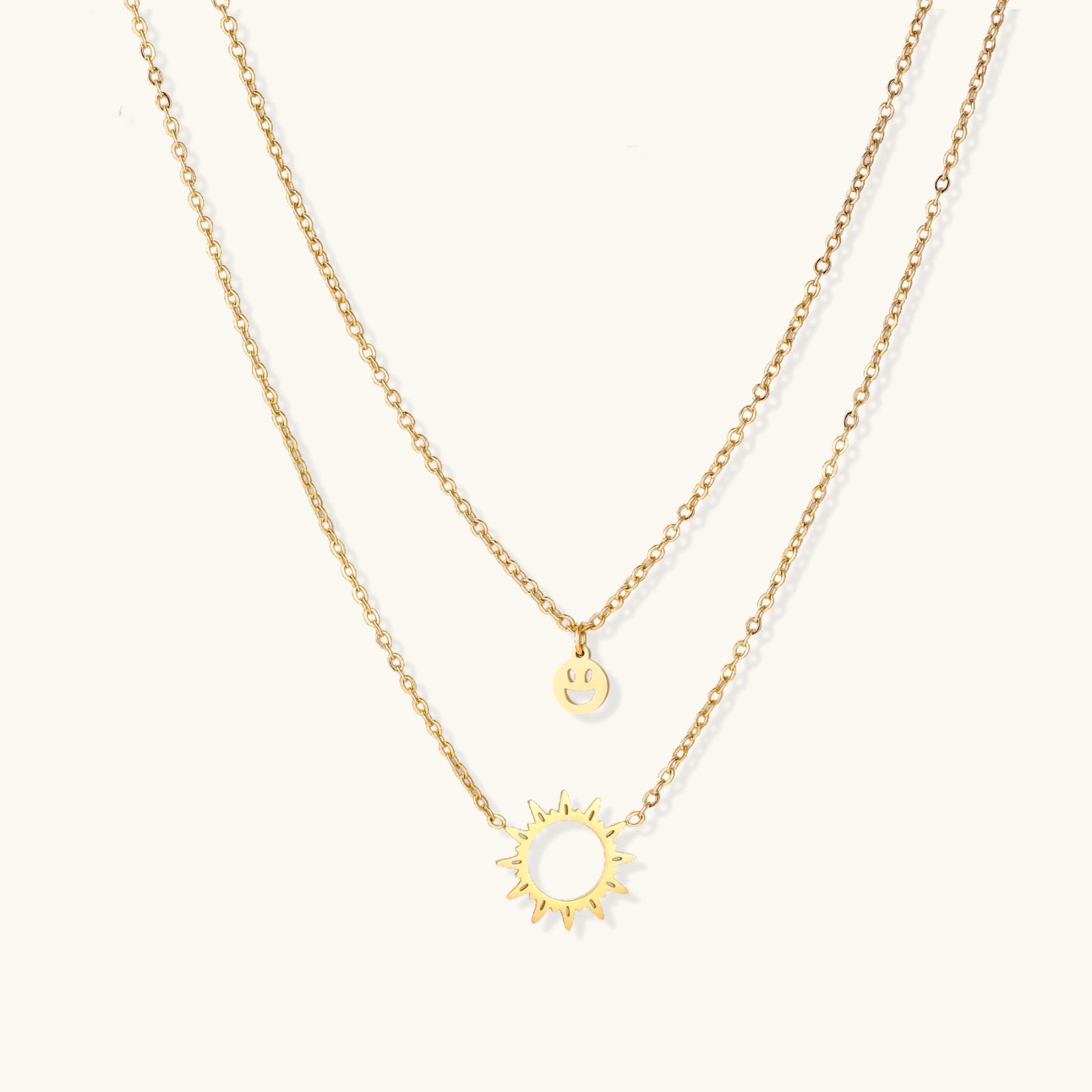 Gold layered necklace set with sunburst and smiley face pendants on delicate chains against white background.